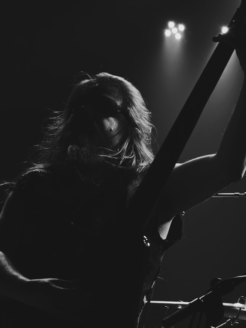 Karhu Kuru, bassist for Ashen Tomb, holding his instrument high and upright in a triumphant pose during an on-stage performance