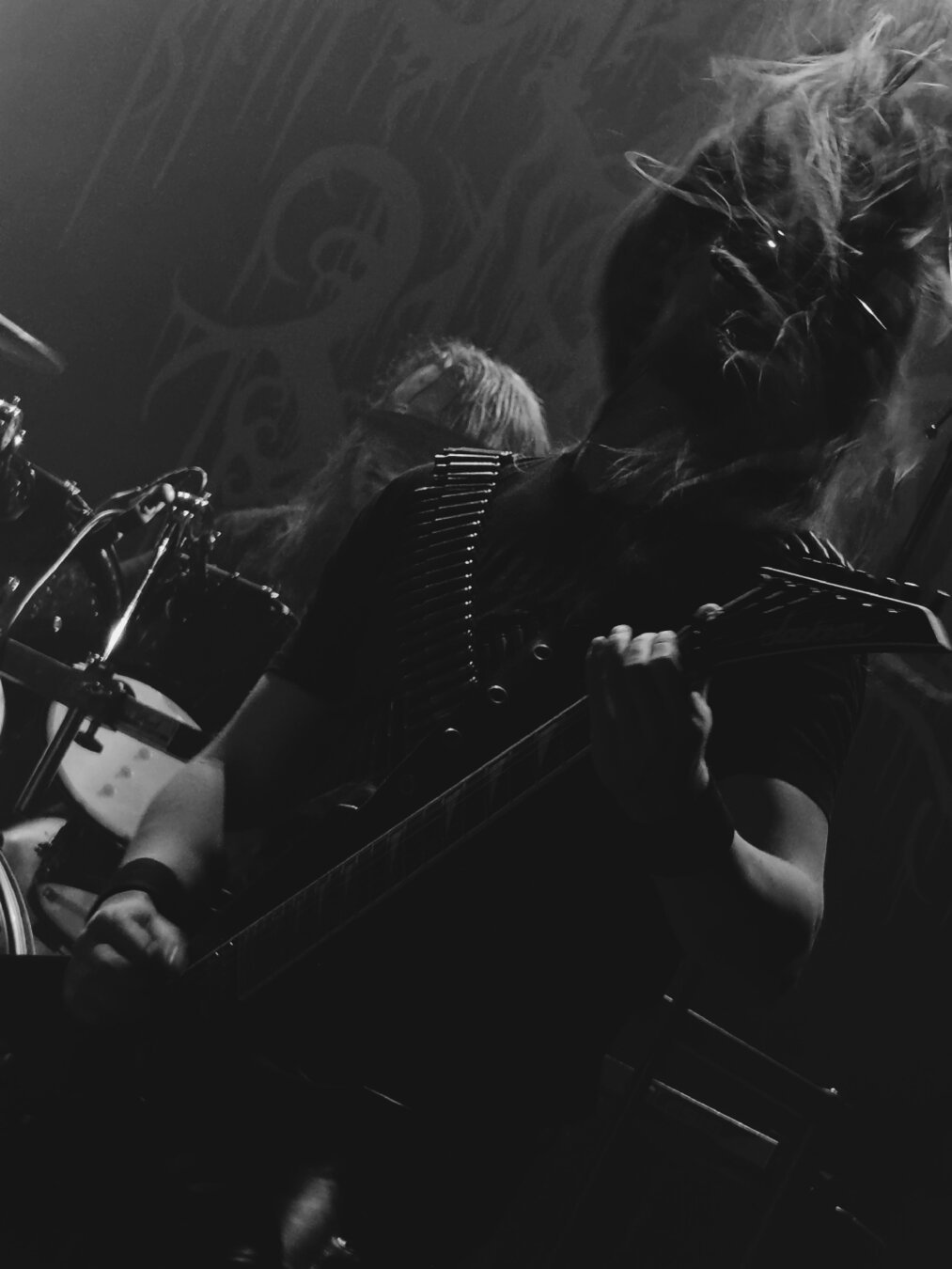 Joonatan Mäkinen getting into it on stage with his guitar while performing with Ashen Tomb, wearing leather pants, sunglasses and two bullet belts crosswise over both shoulders, with his hair flying all over the place