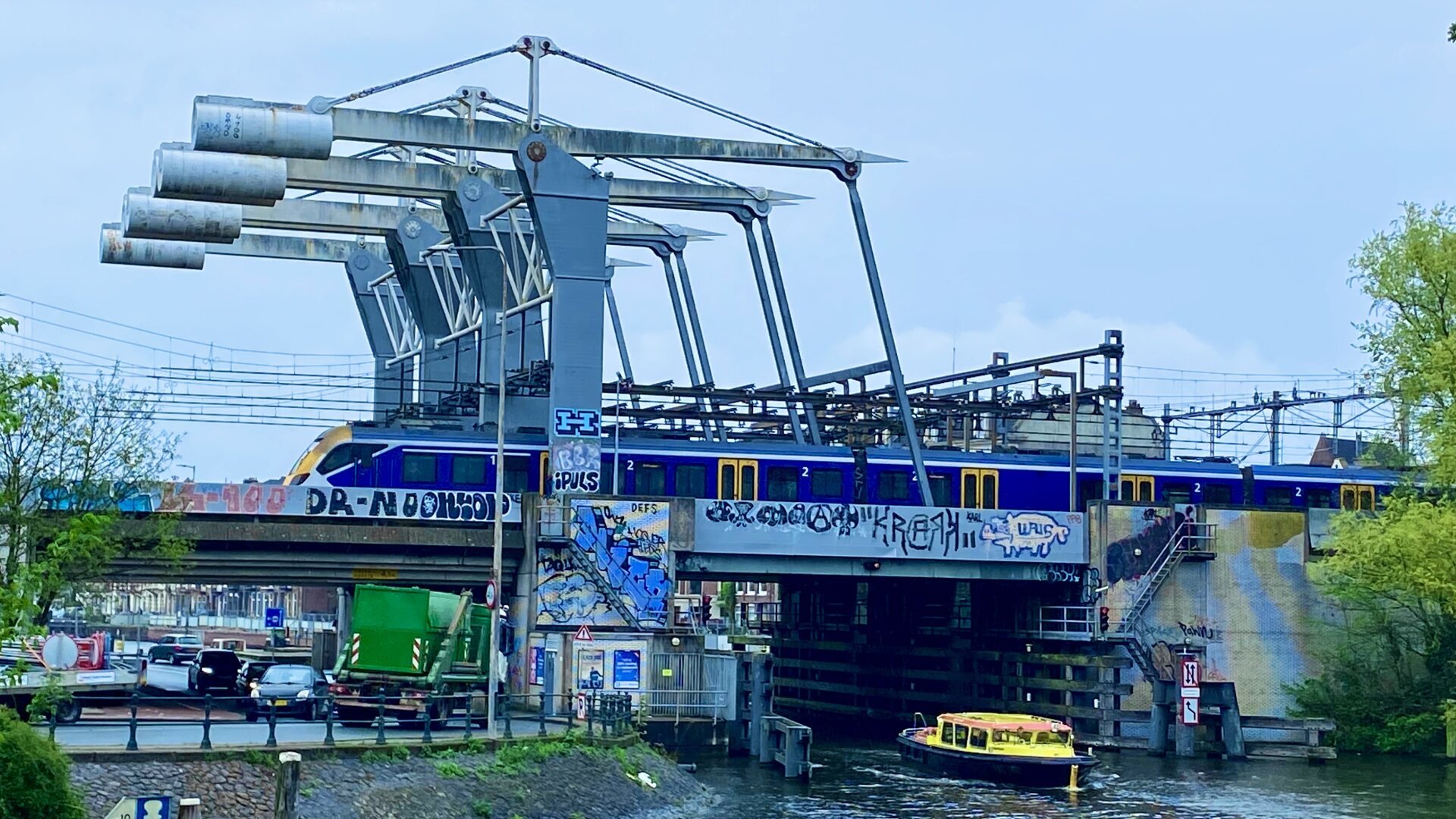 Train moving over a bridge while a yellow boat goes underneath.