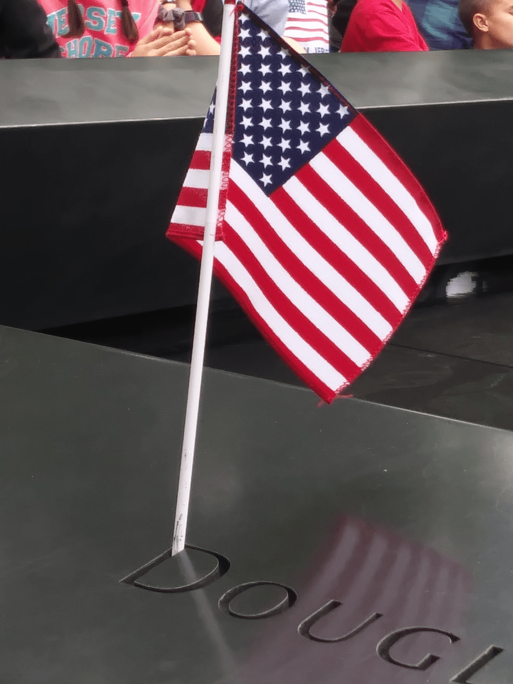 A small American flag placed in the letter of a name inscribed on the bronze parapet with the flag's reflection