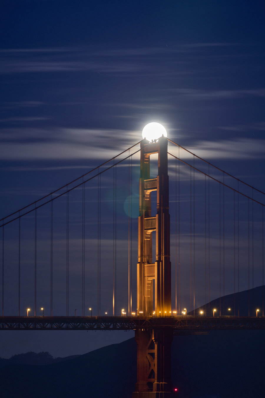 The full moon setting behind the Golden Gate Bridge. The moon is resting on top of one of the bridge towers.