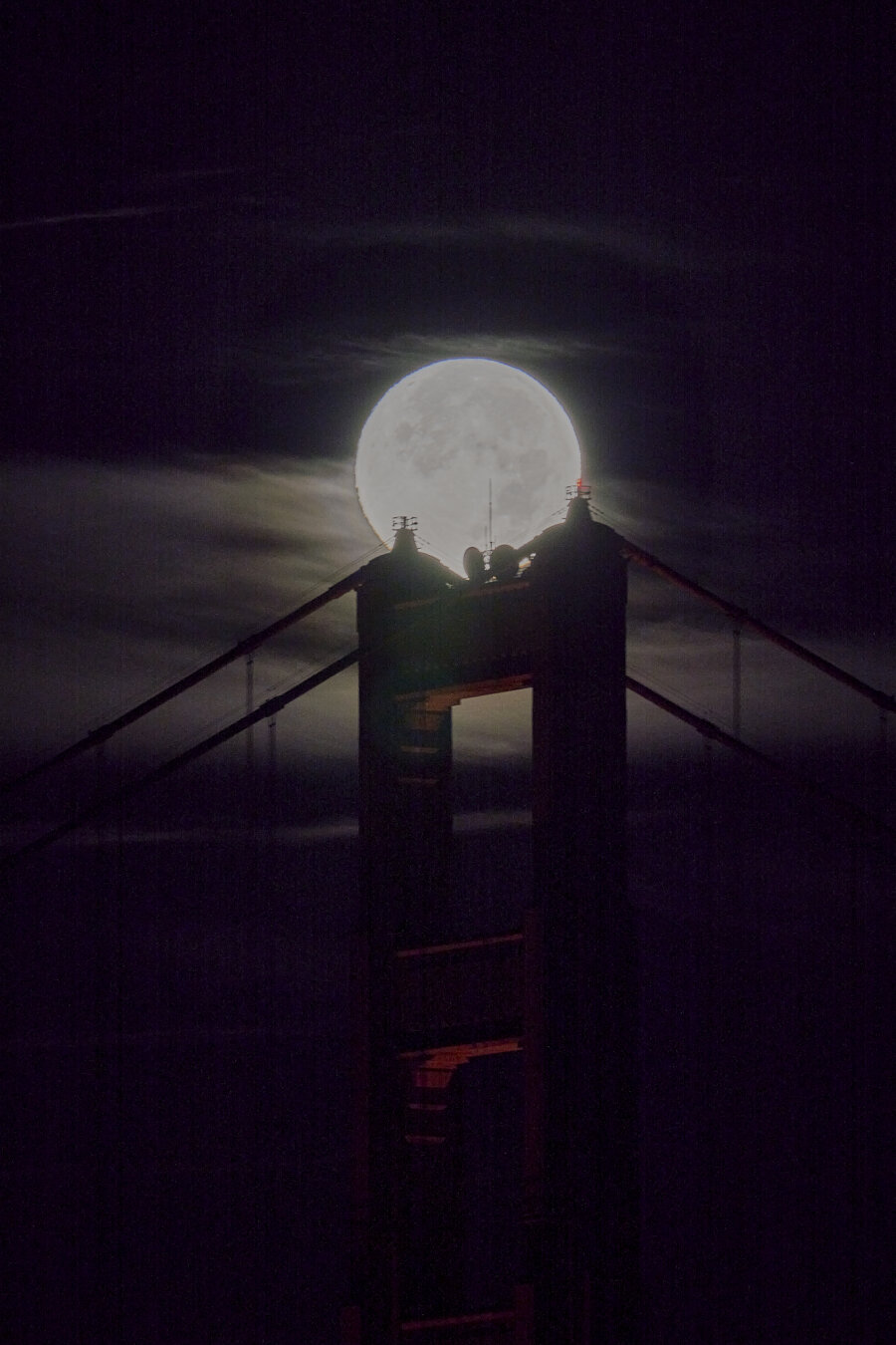 Close up of the full moon setting behind the Golden Gate Bridge. The moon is resting on top of one of the bridge towers.