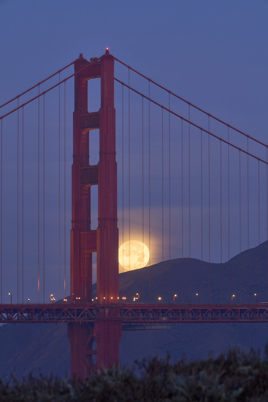 The full moon setting behind the Golden Gate Bridge and about to go behind the hills in the background.