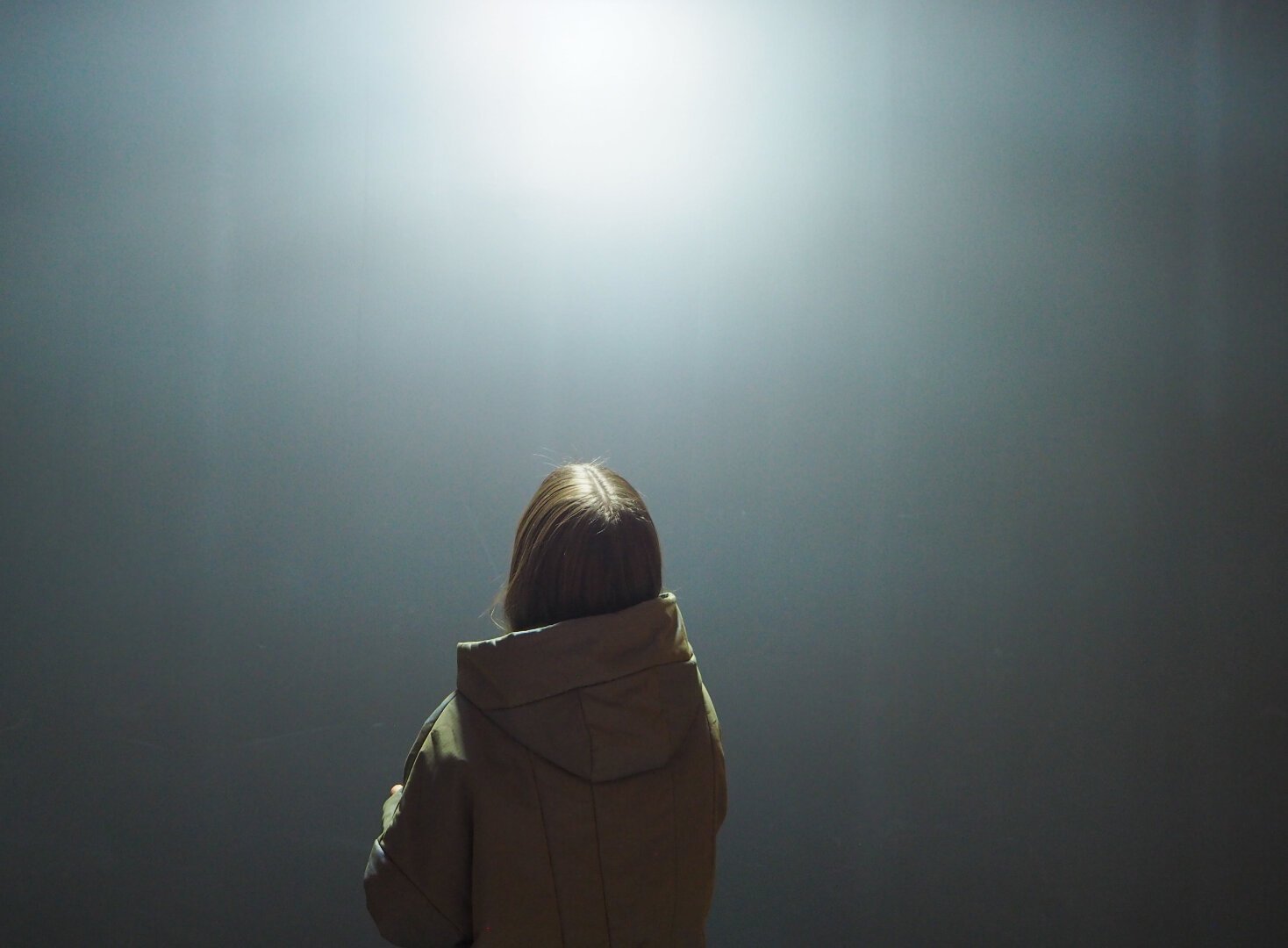 Woman with her back to the camera looks up to an ethereal glow that is part of a museum exhibit.