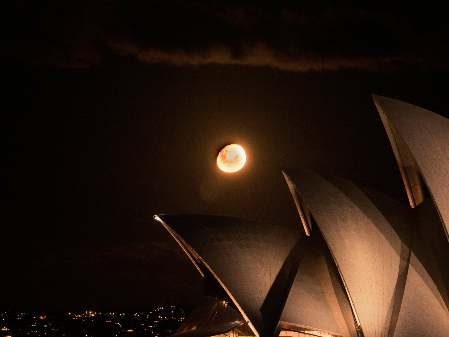 Yellow / Orange full moon rises above the sails of the Sydney Opera House at night