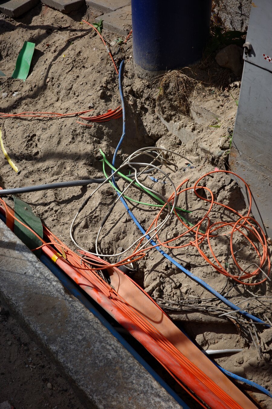 Colourful cables of various kinds (fibreoptic, electrical, etc) laying in the open on sandy ground during urban construction works