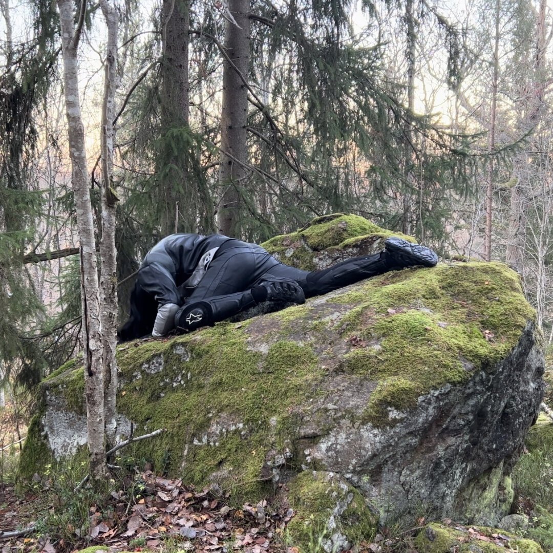 Adam on a rock in the forest, wearing motorcycle gear.