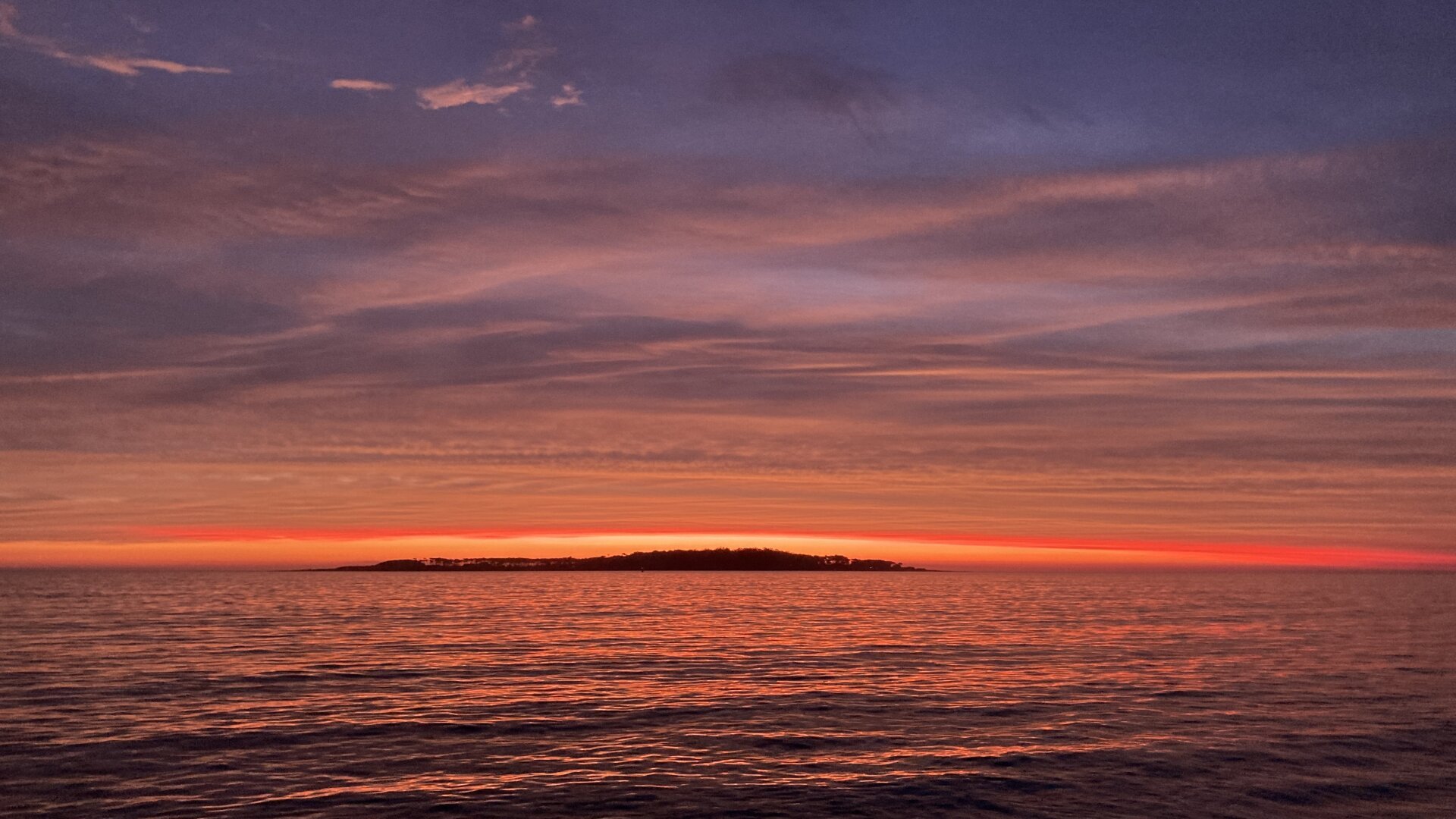 atardecer en tonos de rojos en el mar con una isla de fondo