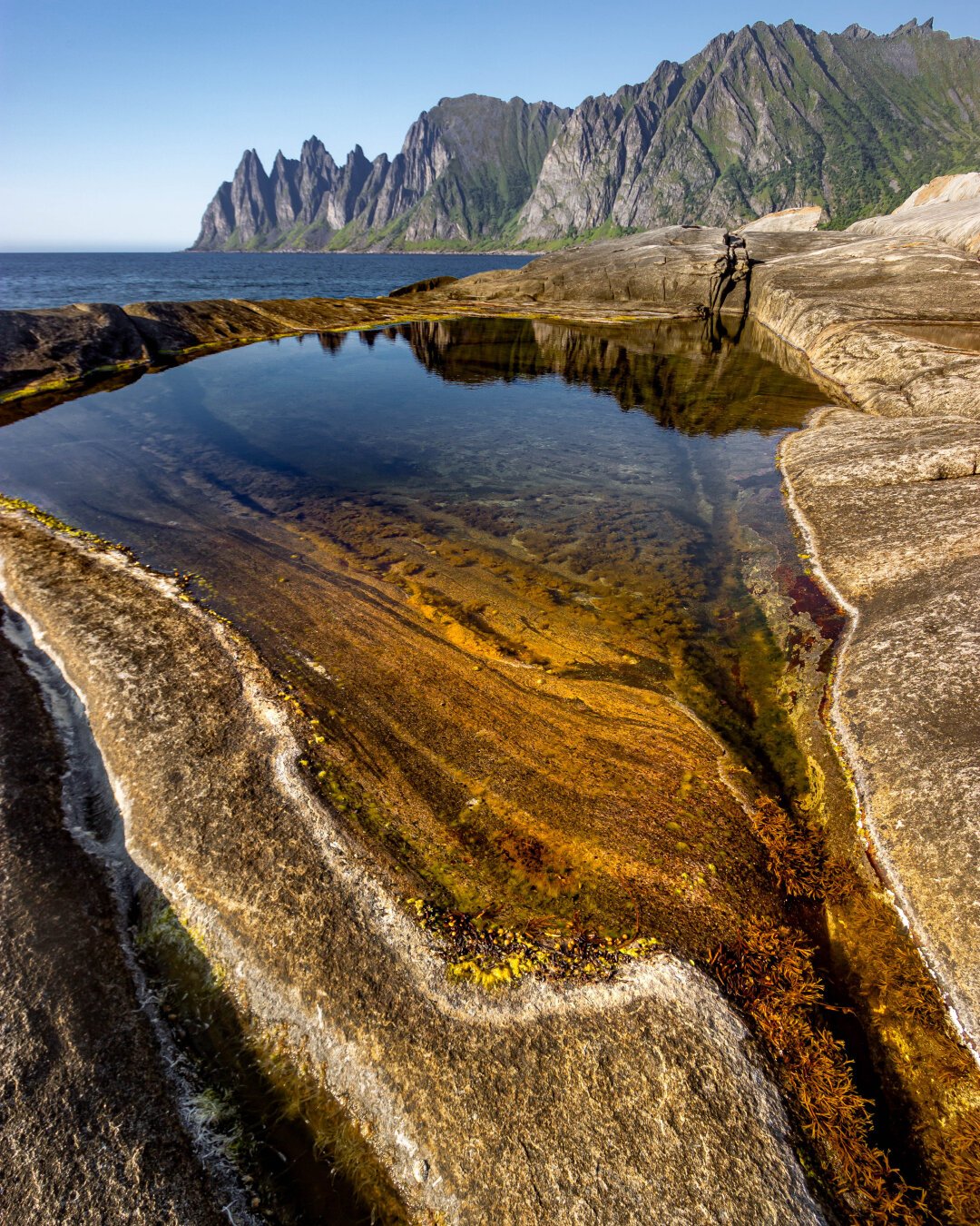 Tungeneset, a pretty puddle on the rocky coast with a mountain in the background