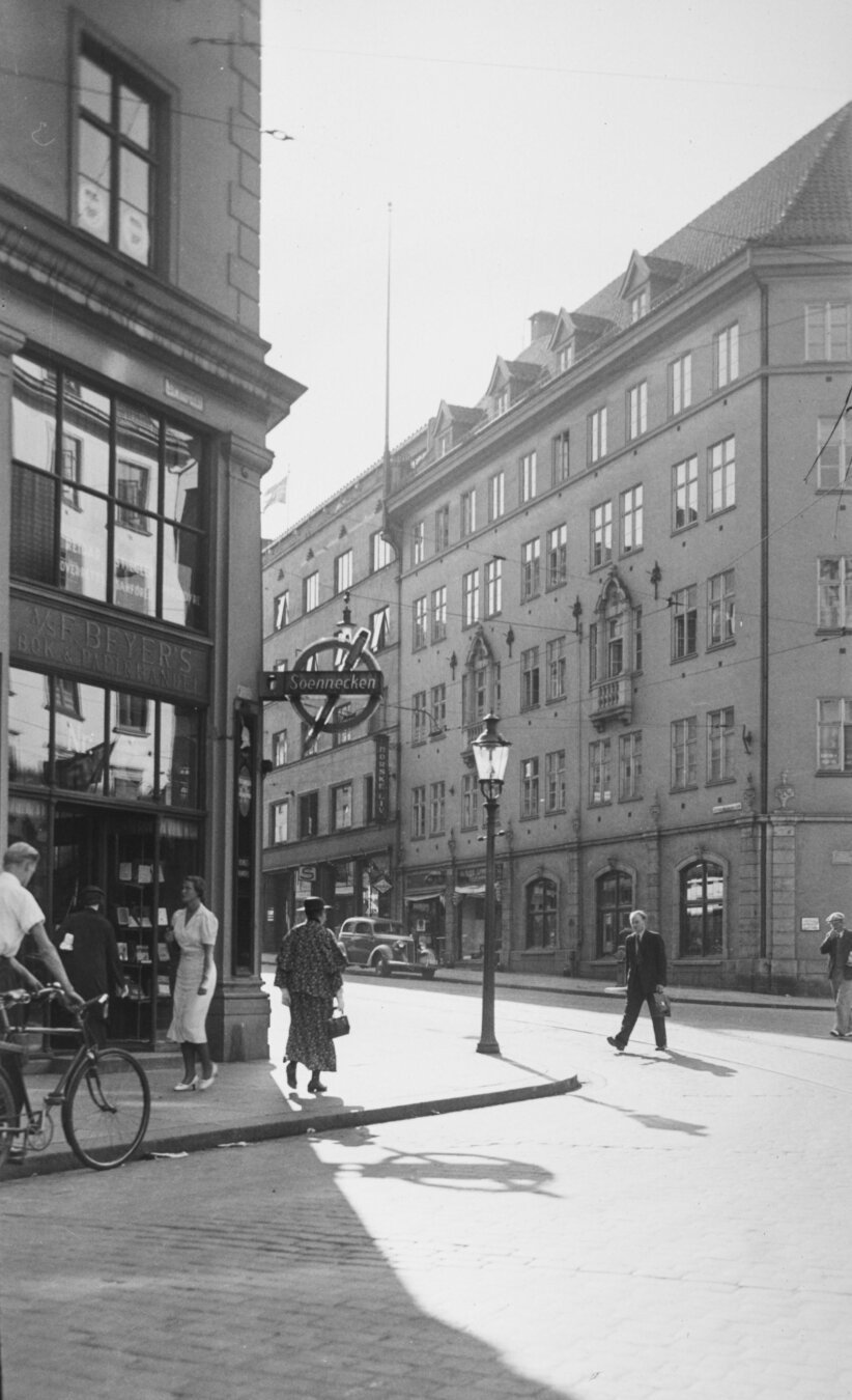 A black and white photo of a Bergen street, people on the sidewalk outside a bookshop with a sign reading 