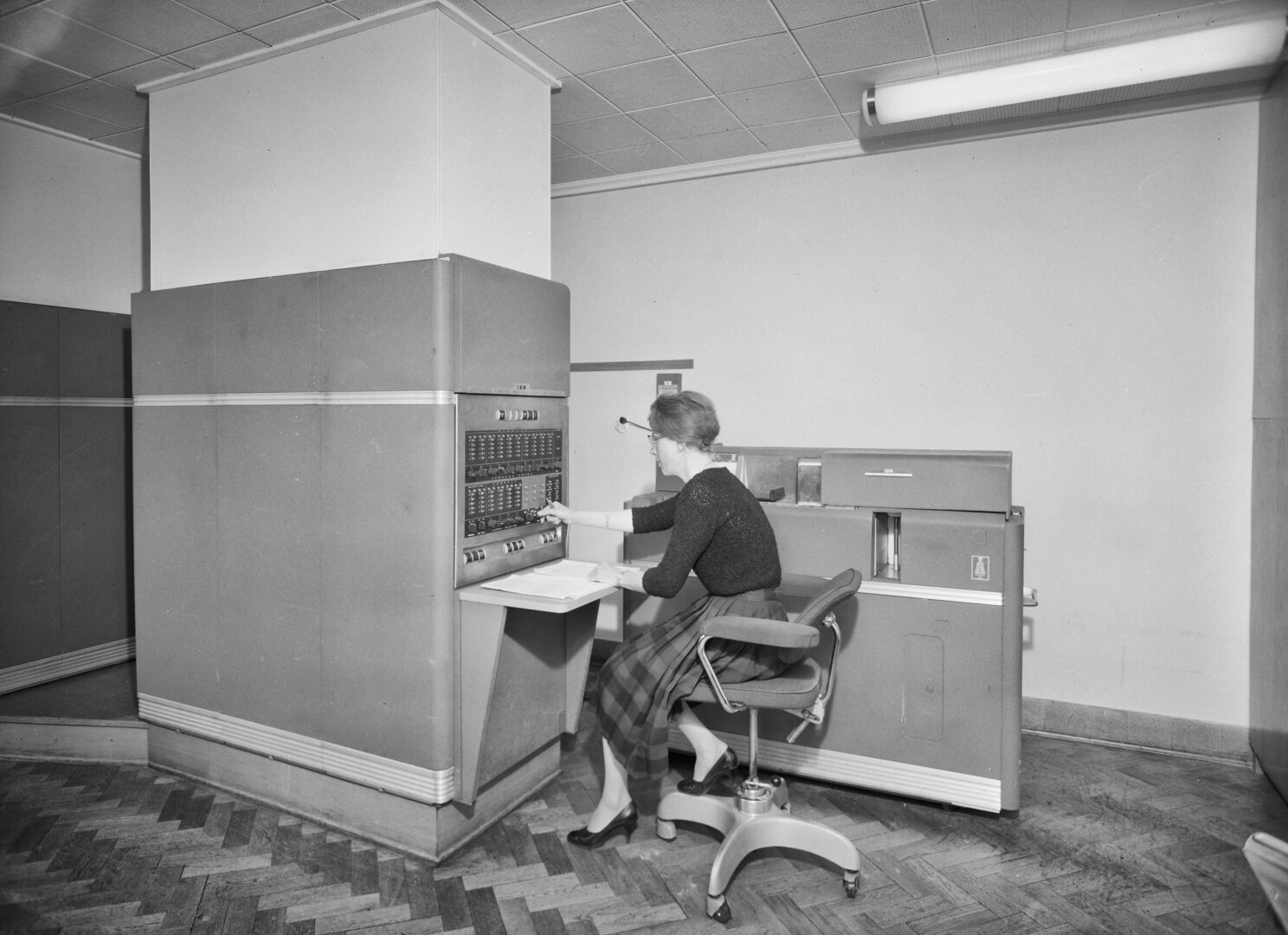 A black and white photo of a woman sitting at an old IBM computer.