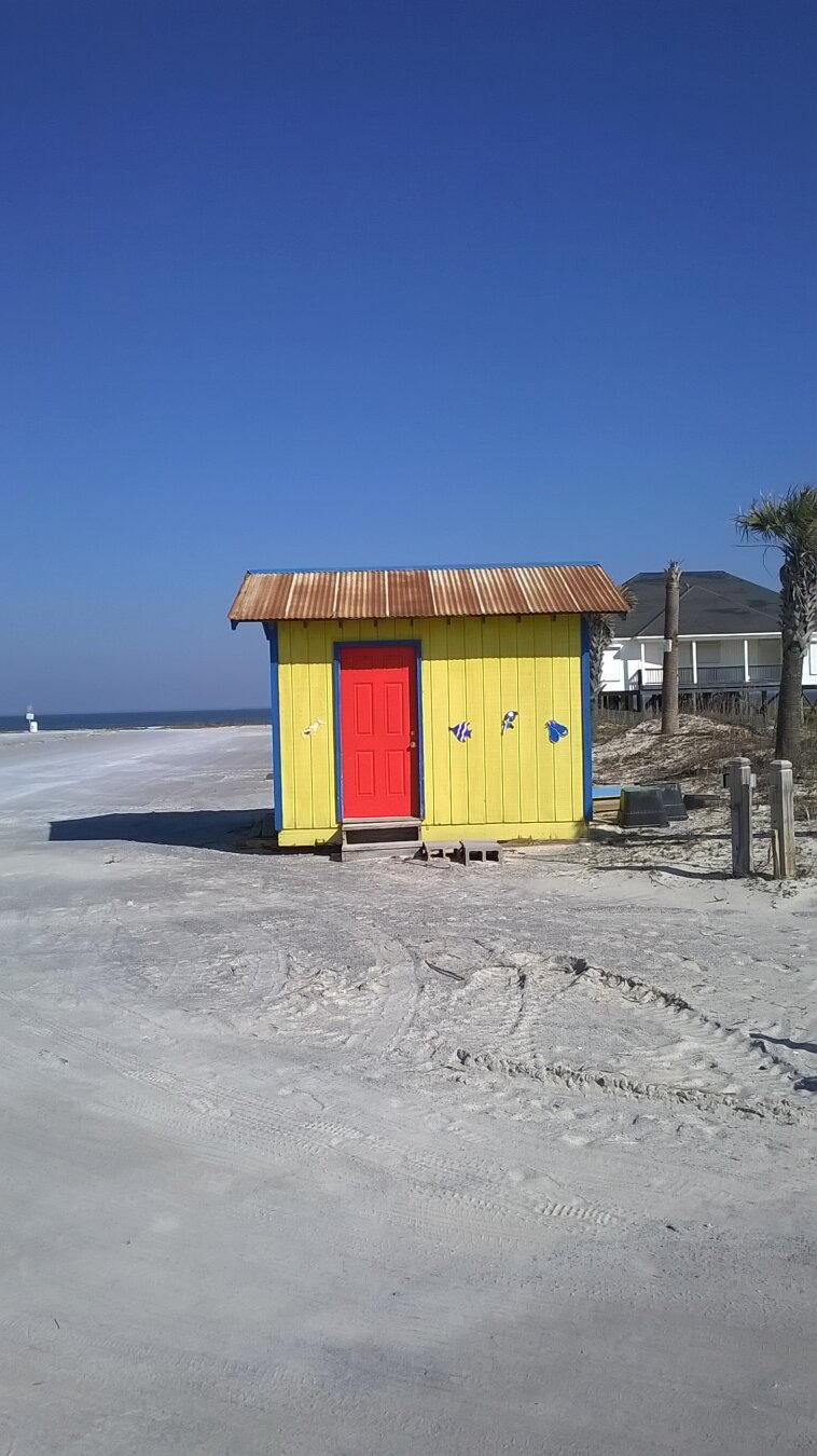 A yellow building with a bright red door, on the beach at Dauphin Island, Alabama.