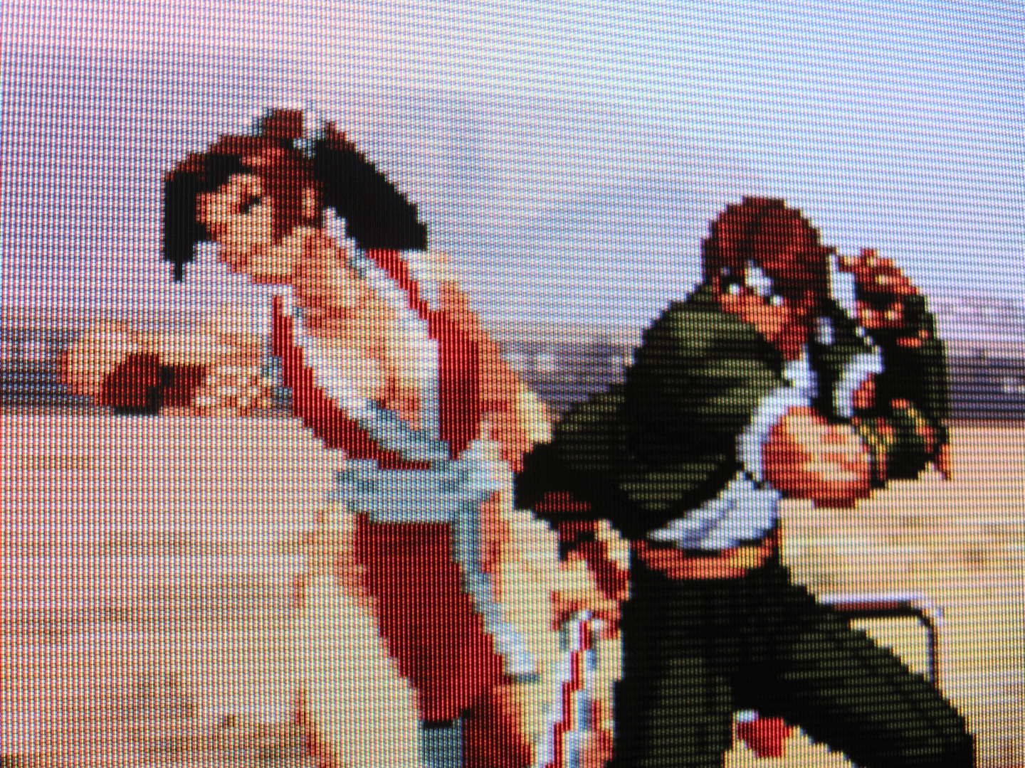 A passenger train listlessly passes by as SNK's Kyo Kusanagi and Mai Shiranui battle intensely in the arid, sun-blasted desert. A well-timed forearm strike makes contact with Mai's jaw, casting her face in intense pain.