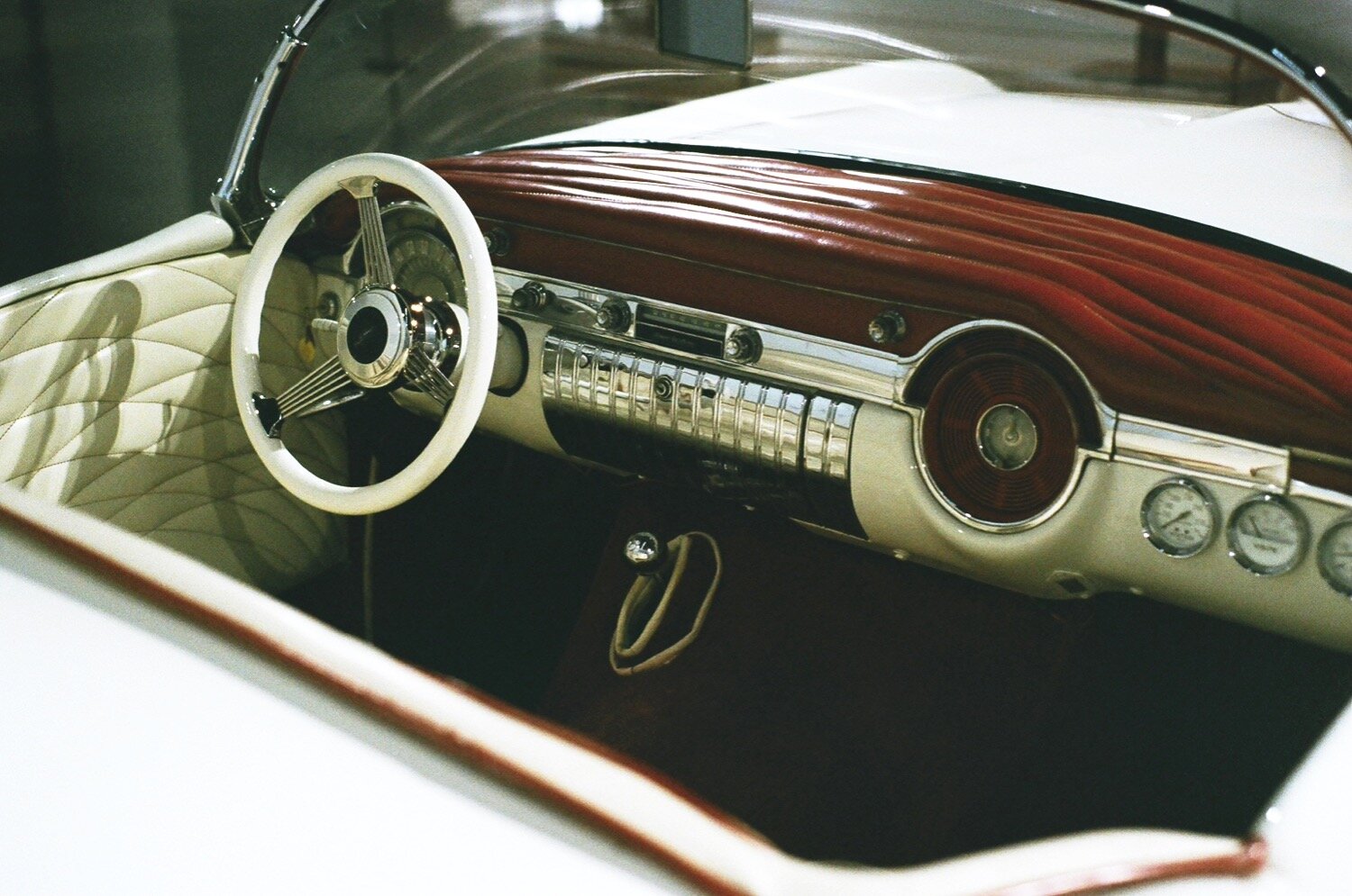 A white classic car with a convertible roof sits under bright museum LEDs. The red velvet interior shines.