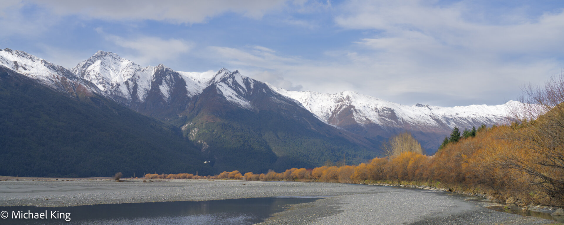 Autumn colours remain in the river valley with snow capped mountains in the distance.