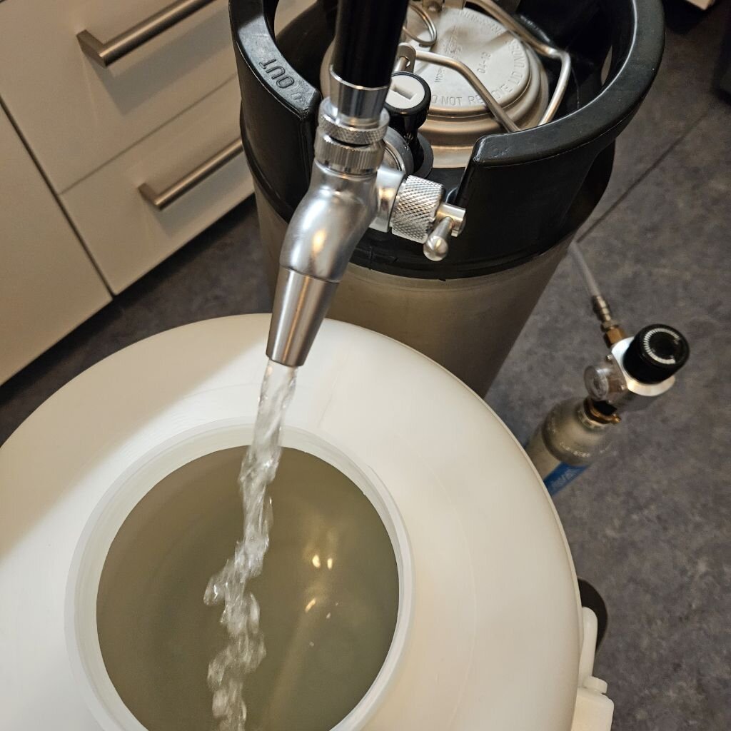 Aus einem Bierhahn an einem Keg fließt Wasser in ein Kunstofffass.