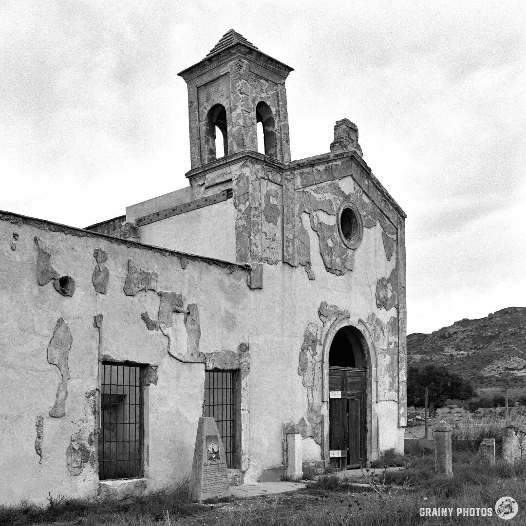 A black-and-white film photo of the front of Cortijo del Fraile, an impressive farmhouse with numerous outbuildings in a remote location, now in a dilapidated state.