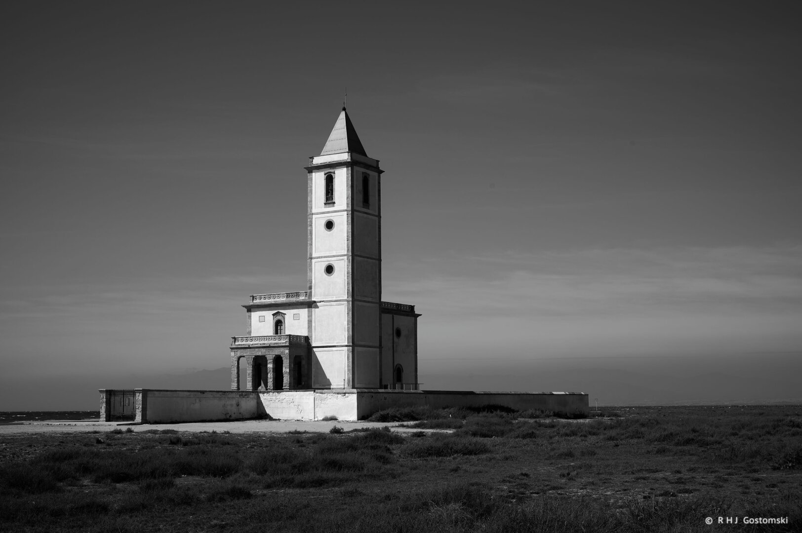 A black-and-white photo of a church in early morning sun in a desolate beach landscape