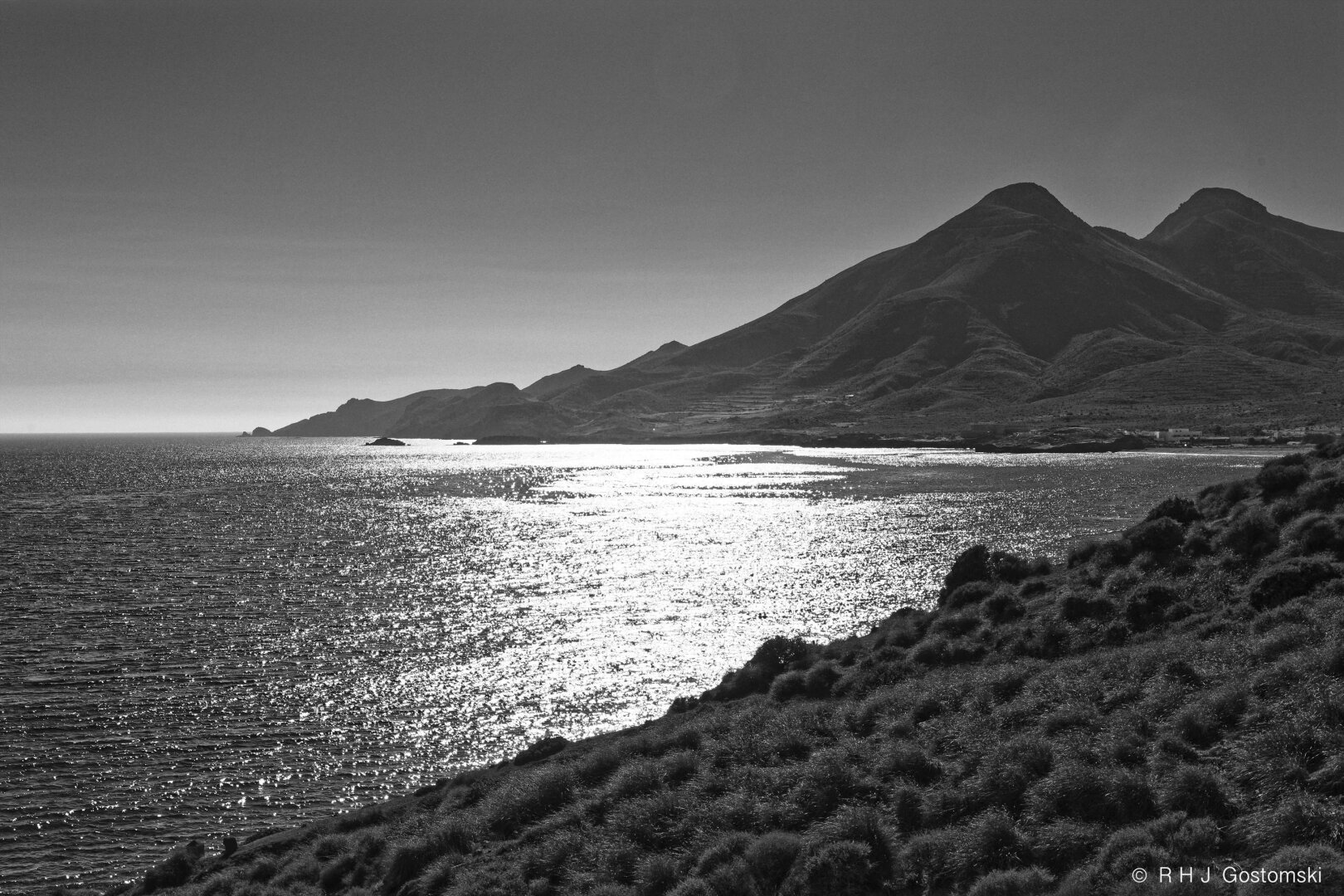 Black-and-white photograph of a sea view from La Isleta del Moro, with a low sun reflecting off the water