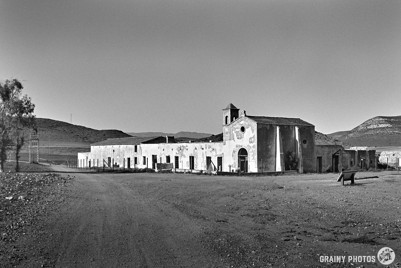 A black-and-white film photo of Cortijo del Fraile, an impressive farmhouse with numerous outbuildings in a remote location, now in a dilapidated state.