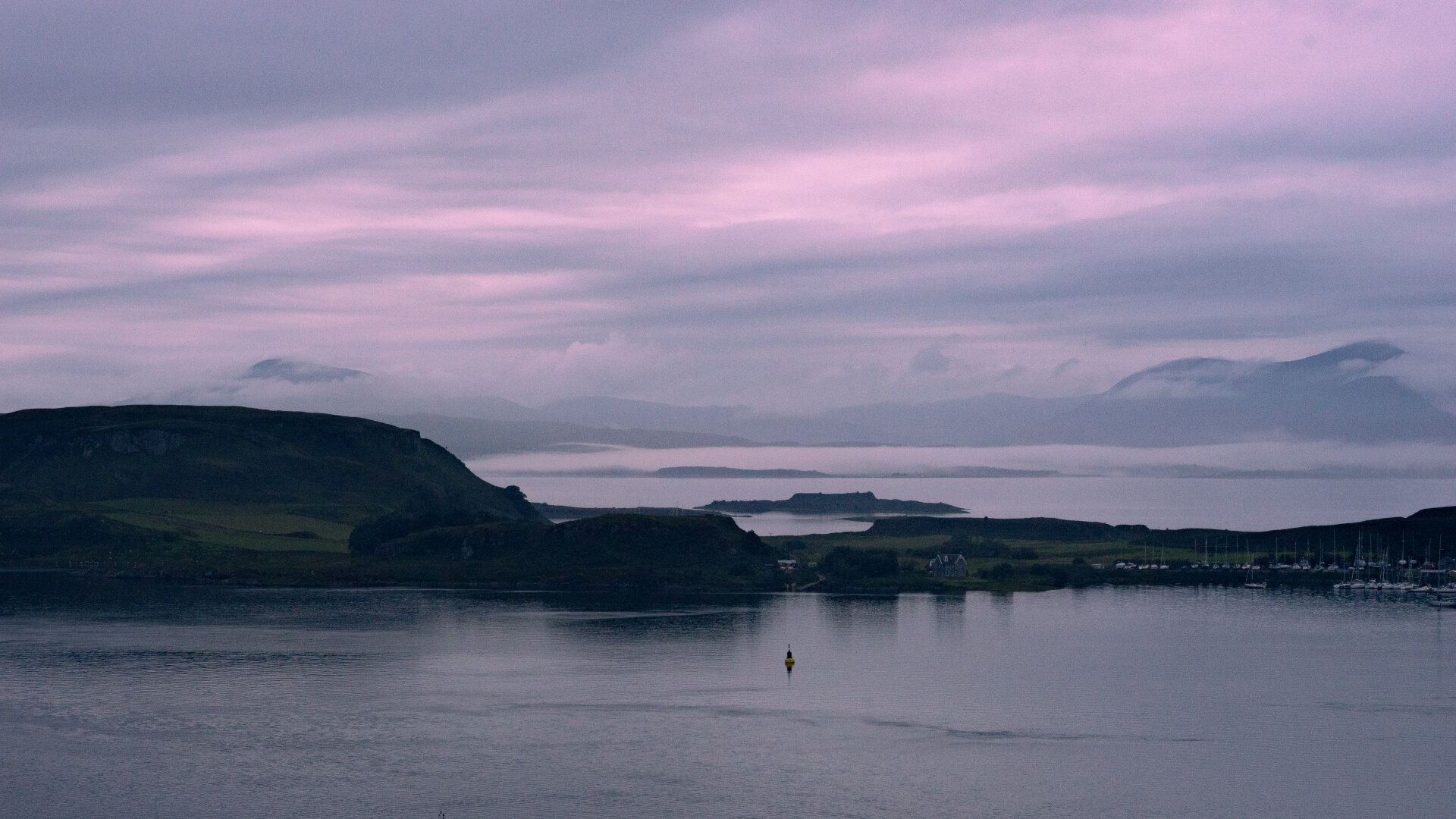 A view of Kerrera from Oban. The photo is in landscape orientation and shows an island covered by low clouds at sunset.