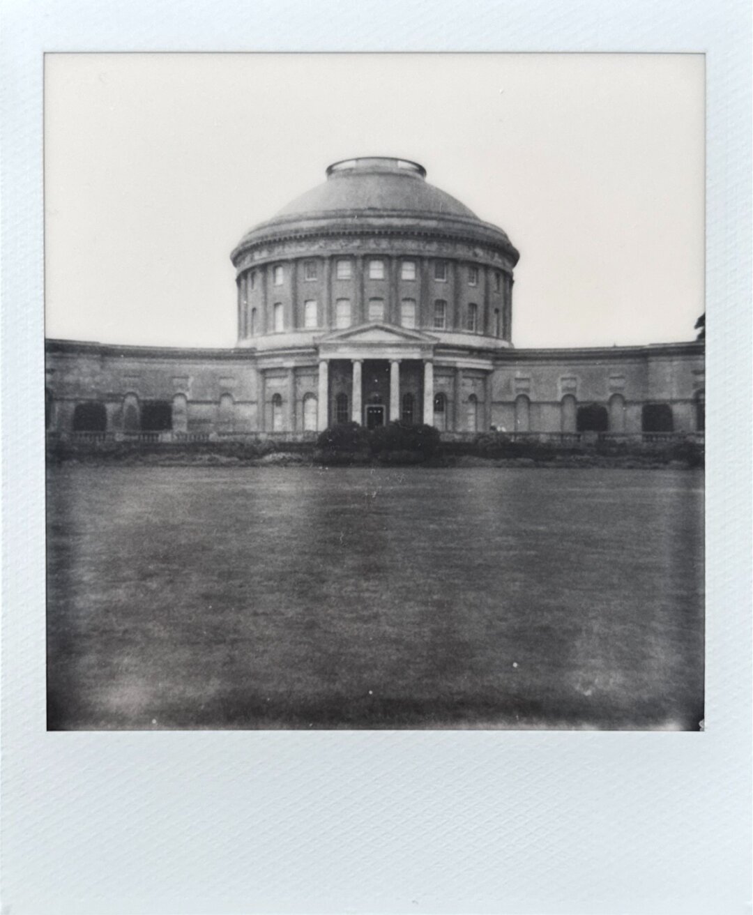A Polaroid photo of Ickworth house in Suffolk, England. The photo shows the neoclassical circular central hall from where the two wings depart. The photo is in black and white. The symmetry of the building is highlighted.
The photo has some discolouration due to the nature of the Polaroid 600 film.