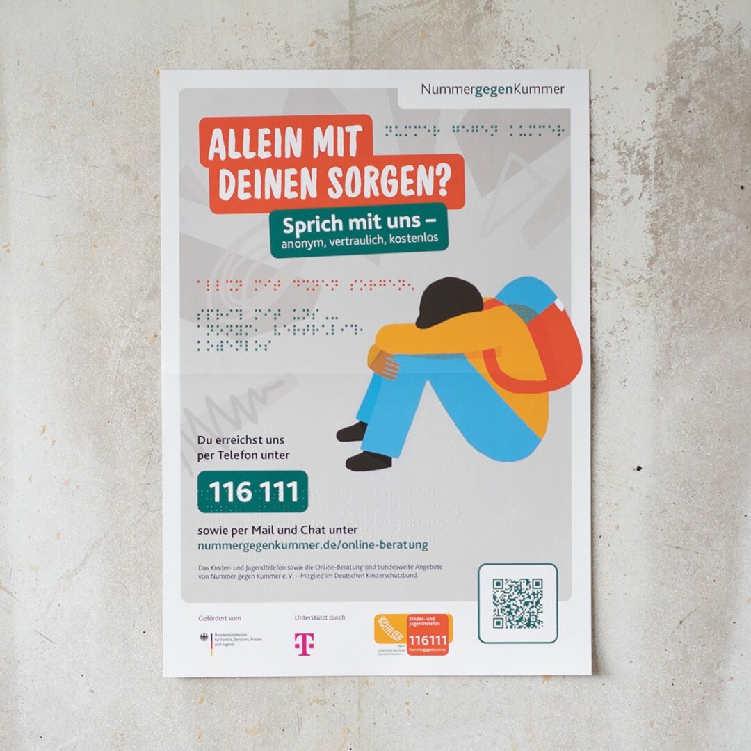 An einer Betonwand hängt das Plakat der Nummer gegen Kummer, das ich gestaltet habe. Daneben steht auf einem schwarzen Balken die Überschrift „Design-Portfolio”. Das Plakat ist sowohl visuell als auch taktil gestaltet.