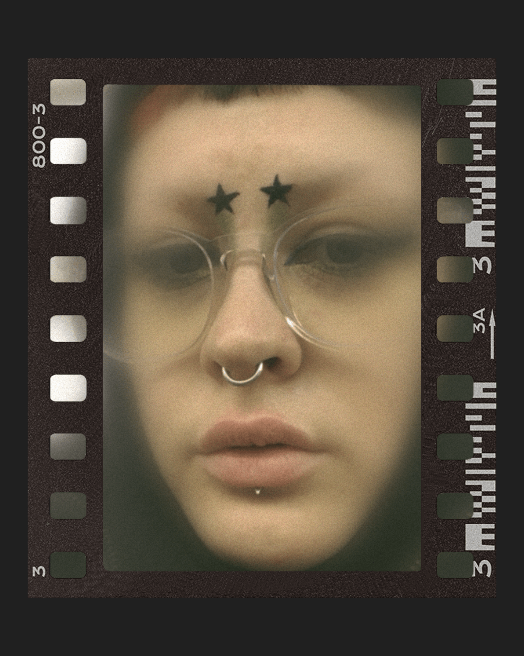 Eine Nahaufnahme von Marias Gesicht, um deren Make Up des Tages zu zeigen. Statt Augenbrauen befinden sich Sterne an der Stelle. Dey trägt eine große Brille und bisschen grünes Make Up mit schwarzem Eyeliner.