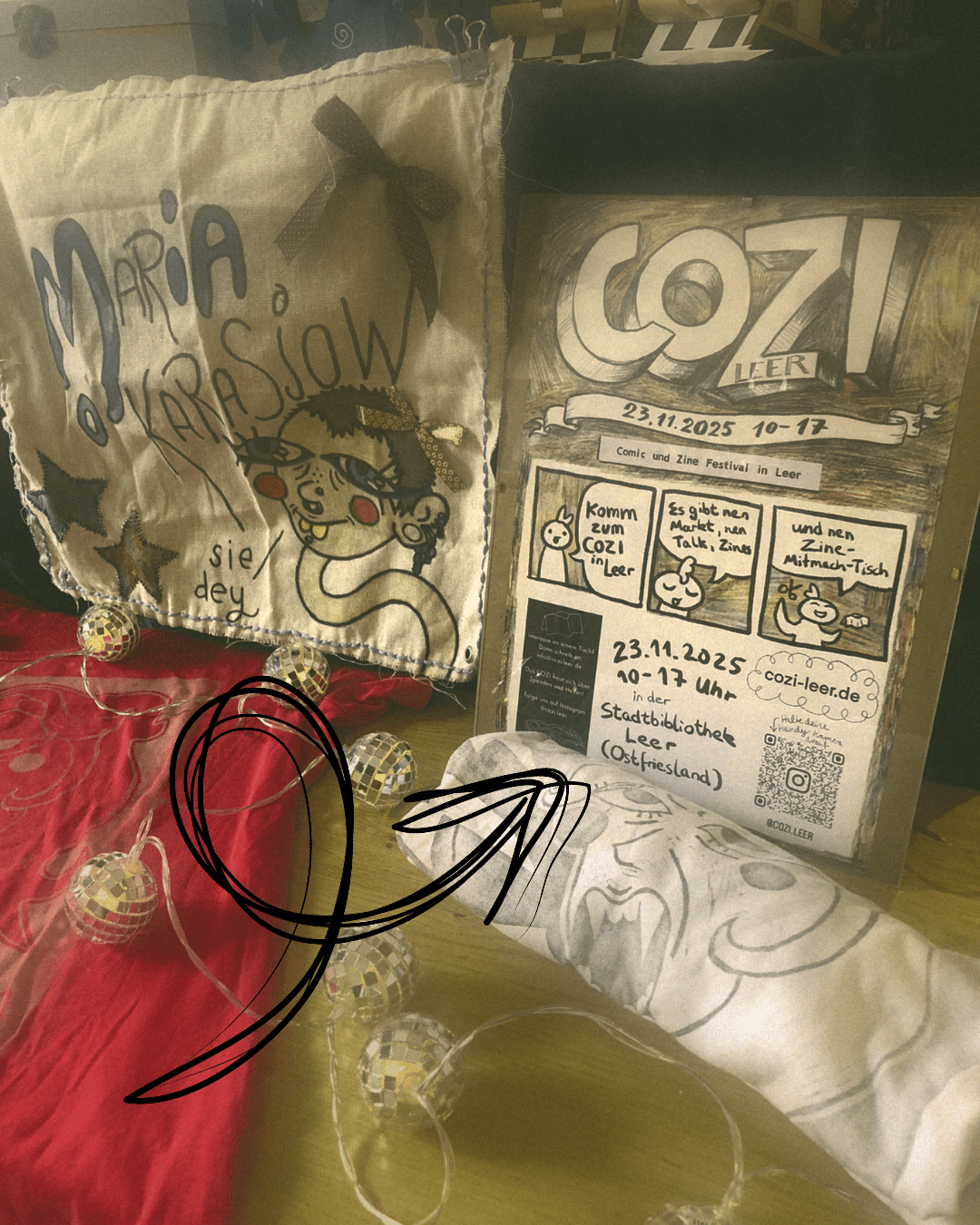 Nahaufname vom unteren Bereich des Markt Tisches von Maria. Es zeigt ein Pfeil auf das Poster vom COZI Fest. Dort wird dey als nächstes ausstellen.