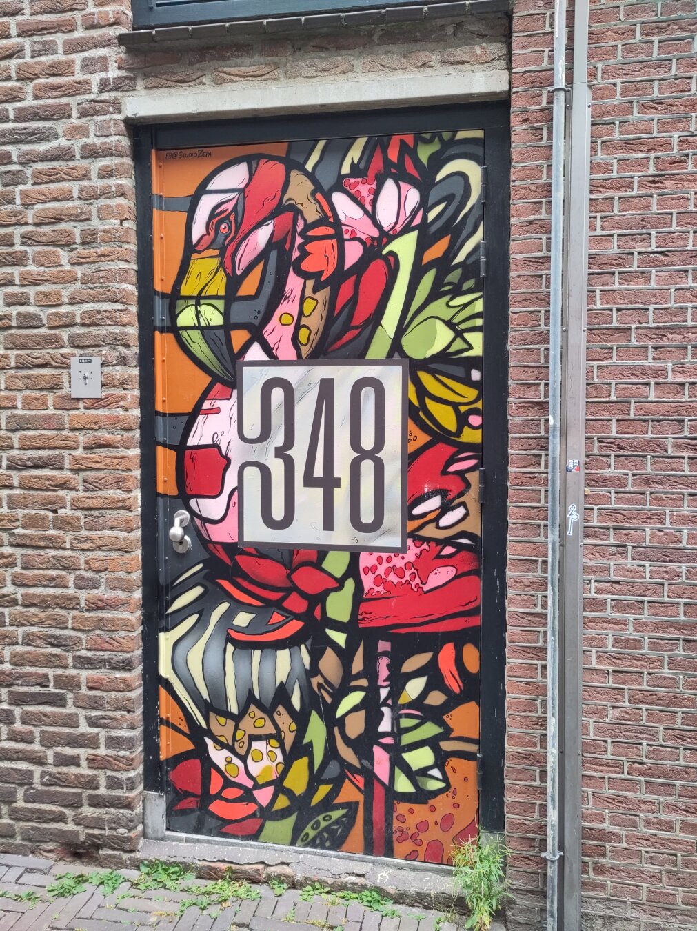 A colourful painted, mosaic-like door, depicting a flamingo and flowers. The number 348 is written in a seperate box in the middle of the door.