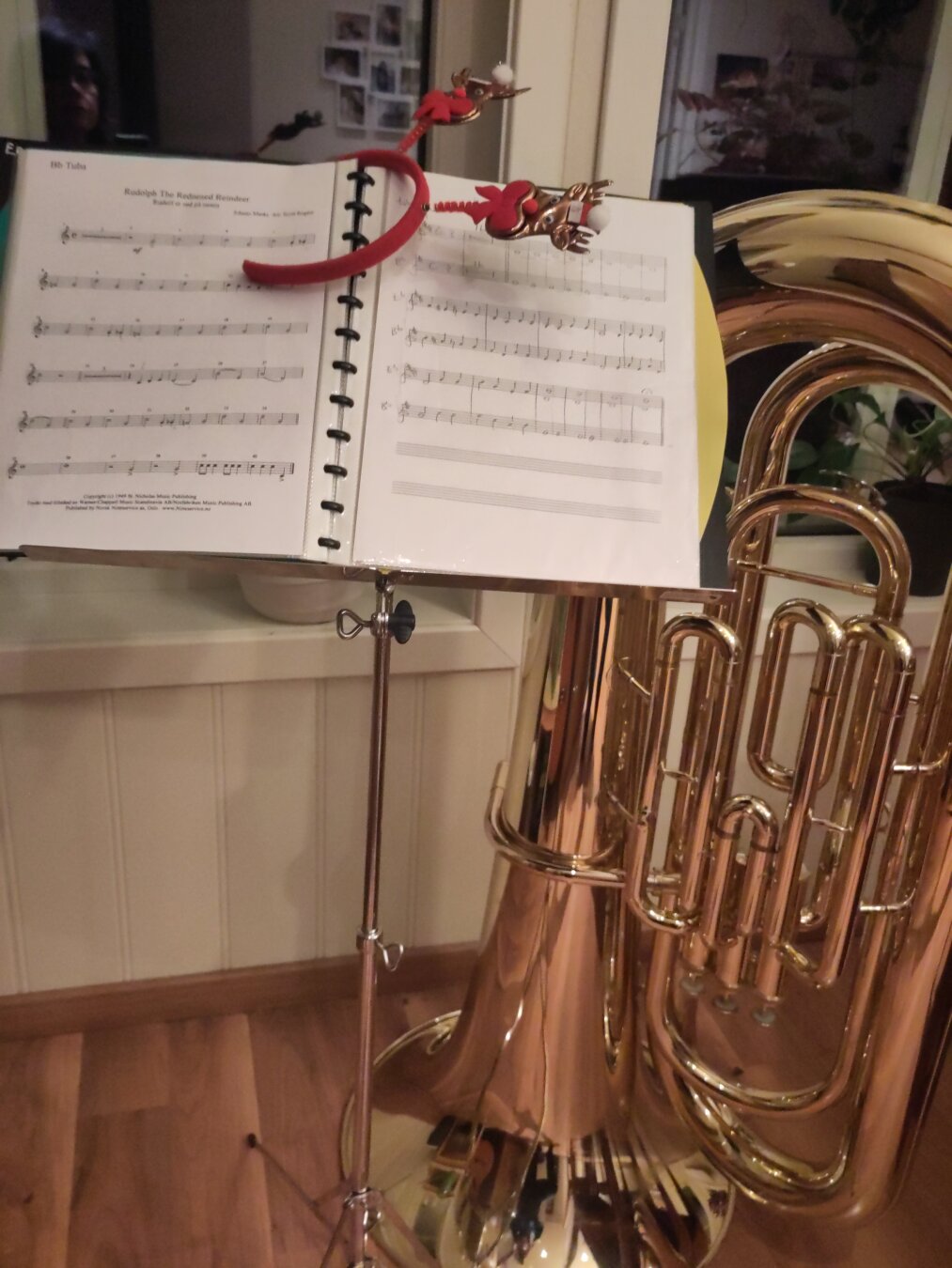 A music stand with notes for Rudolph the red nosed reindeer, a hairband with reindeer and a tuba