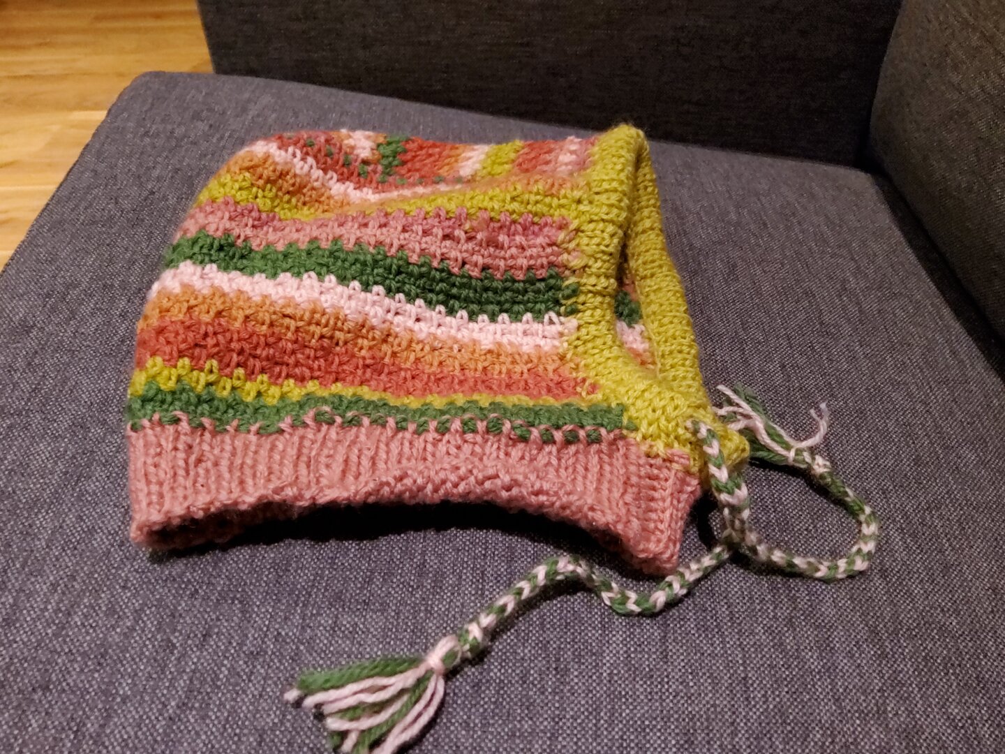 A colourful and finished crocheted balaclava on a gray sofa