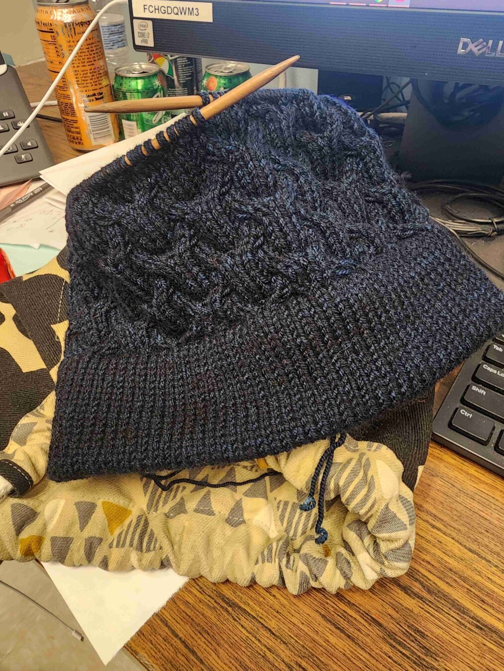 An in progress dark blue cabled hat on an office desk