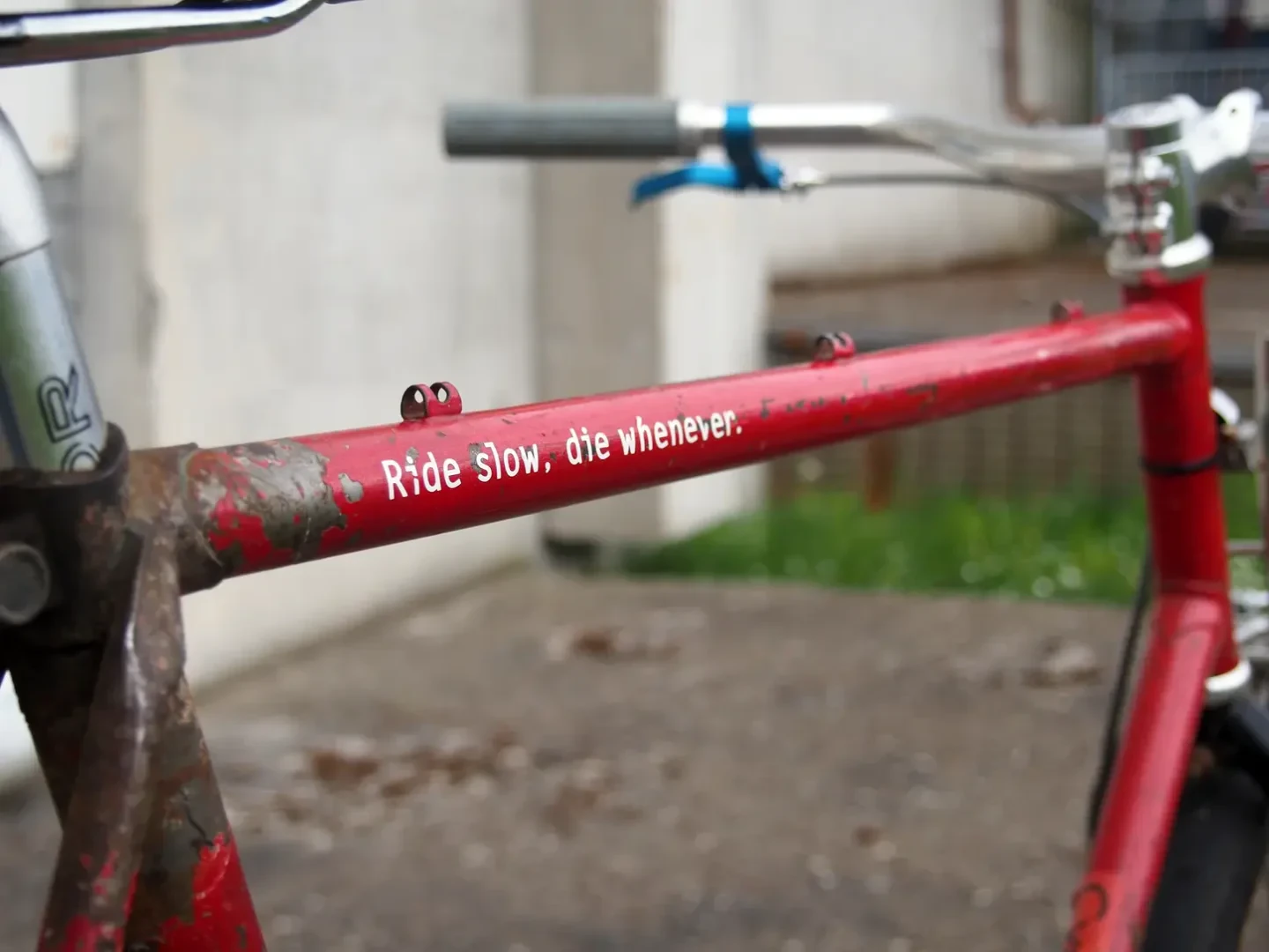 Decal reading "ride slow, die whenever" on a rusty top tube of a bicycle.
