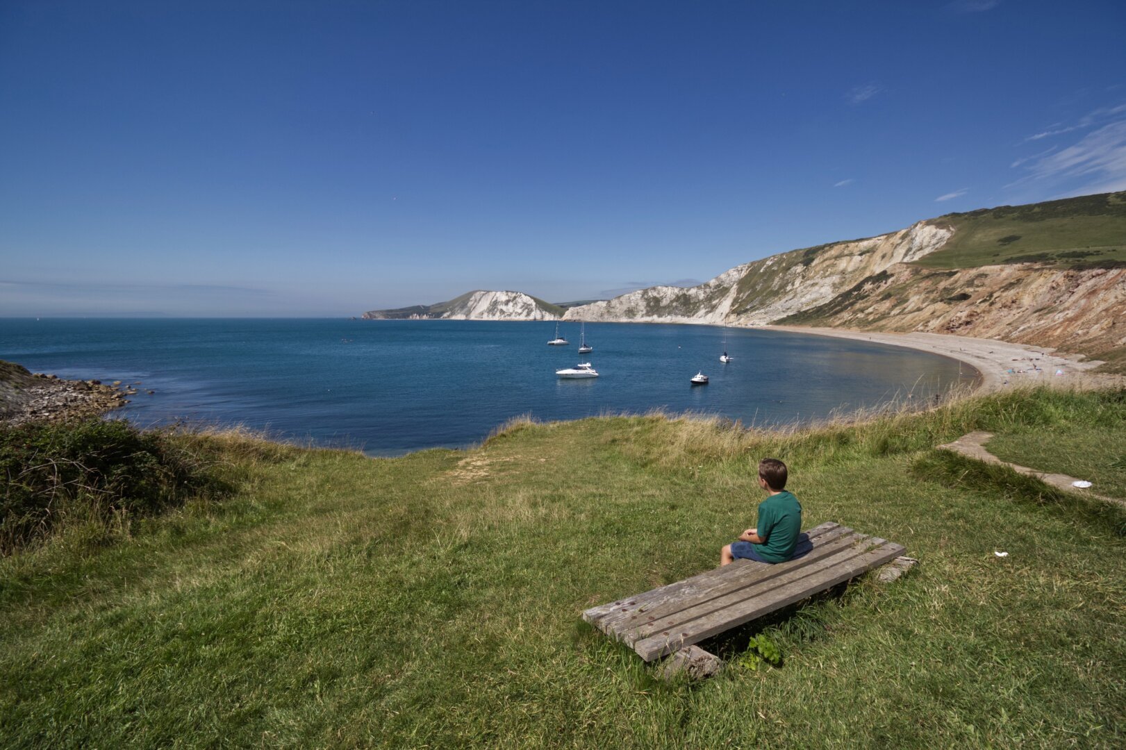 A boy sitting on a bench looking at Worbarrow Bay