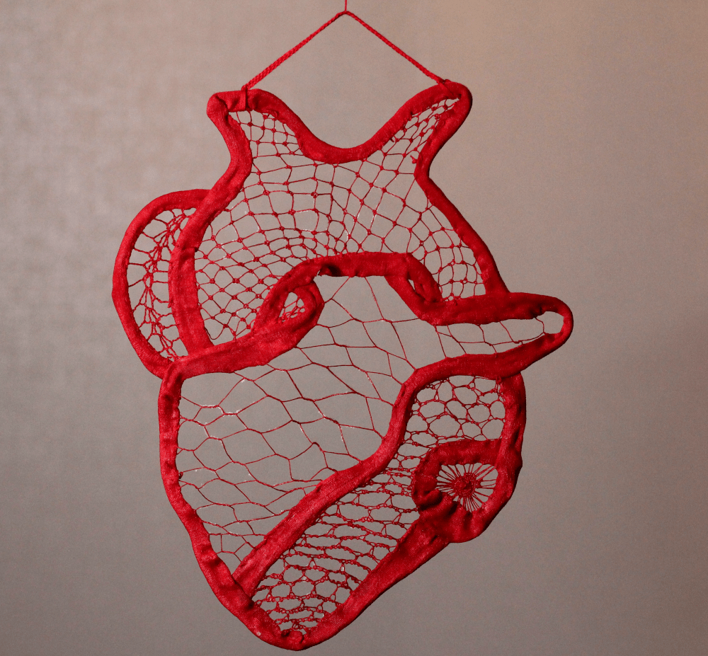 A red heart, somewhat anatomically correct, made with sewn lace, hanging from a string at the top