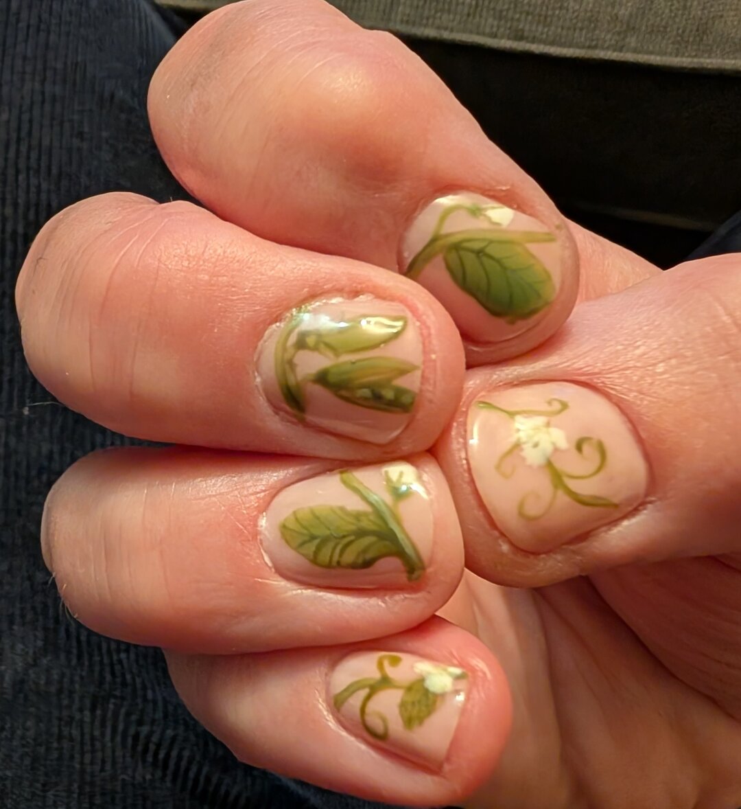 My bent fingers show off my new manicure. My nails have a pale neutral background, on them are painted details of a pea plant vine with it's leaves, flowers, & two peapods with teeny tiny peas inside.