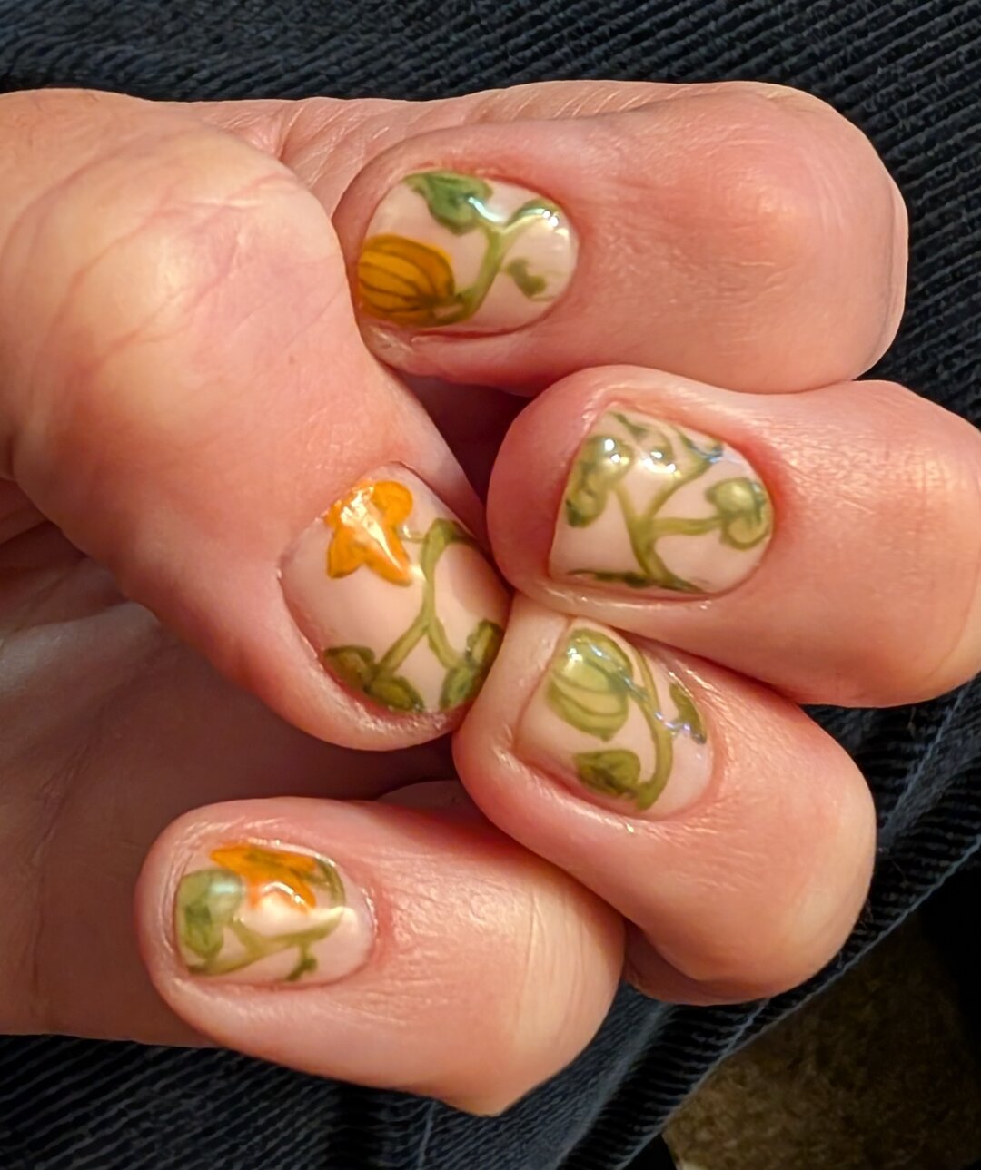 The bent fingers of my other hand show the same pale neutral background, with a pumpkin plant vine.  There are orange pumpkin flowers, and there are two tiny pumpkins.