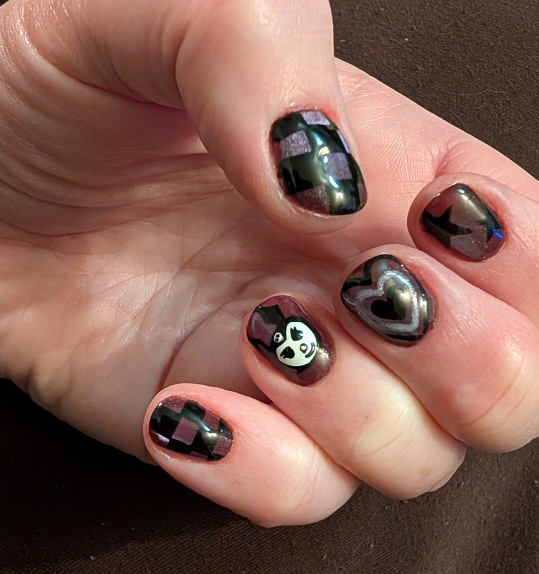 New nail art. My nails have a purple cat's eye effect background, with (predominantly) black nail art . They have: checkerboard, hearts, stars, & a Kuromi face  on top.