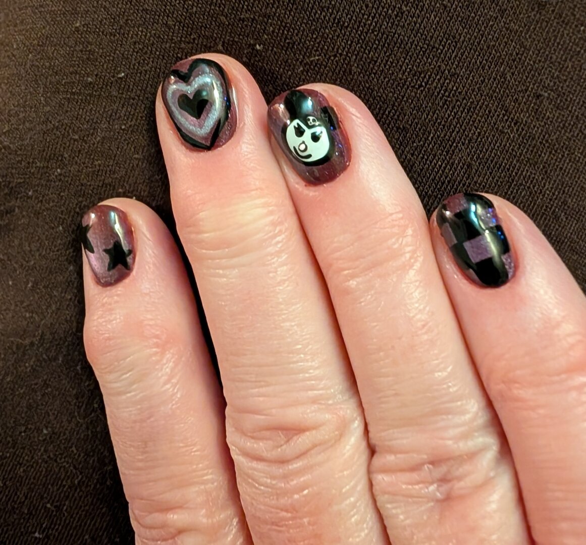 Nail art. A purple cat's eye effect background, with (predominantly) black nail art. Stars, heart, checkerboard, & a Kuromi face.