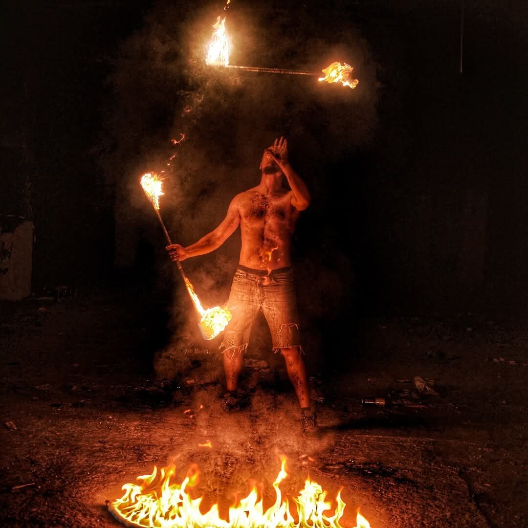 "A fire performer juggling flaming props at night, surrounded by smoke and a ring of fire on the ground."