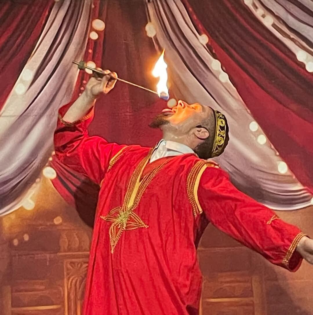 "A fire performer dressed in a red traditional outfit, skillfully fire-eating on stage with a theatrical backdrop."