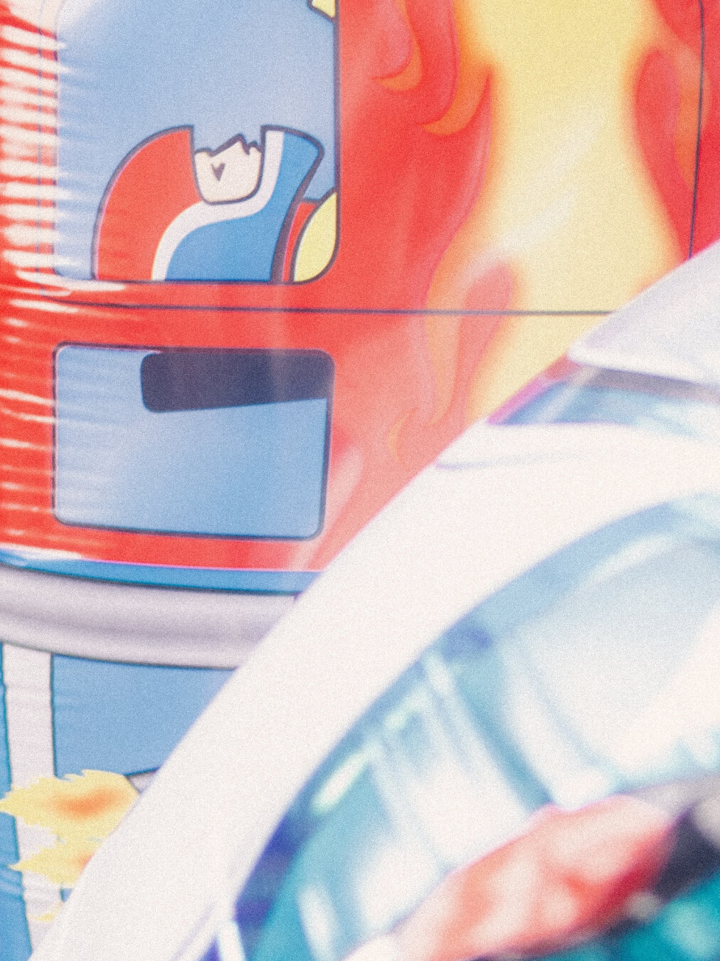 A textured, graphic macro close-up of colorful foil balloons with a fine film grain. A vibrant red, yellow, and orange cartoon fire truck illustration dominates the upper frame, contrasted against the clean, translucent cyan and white curve of an inflatable rocket balloon in the foreground.