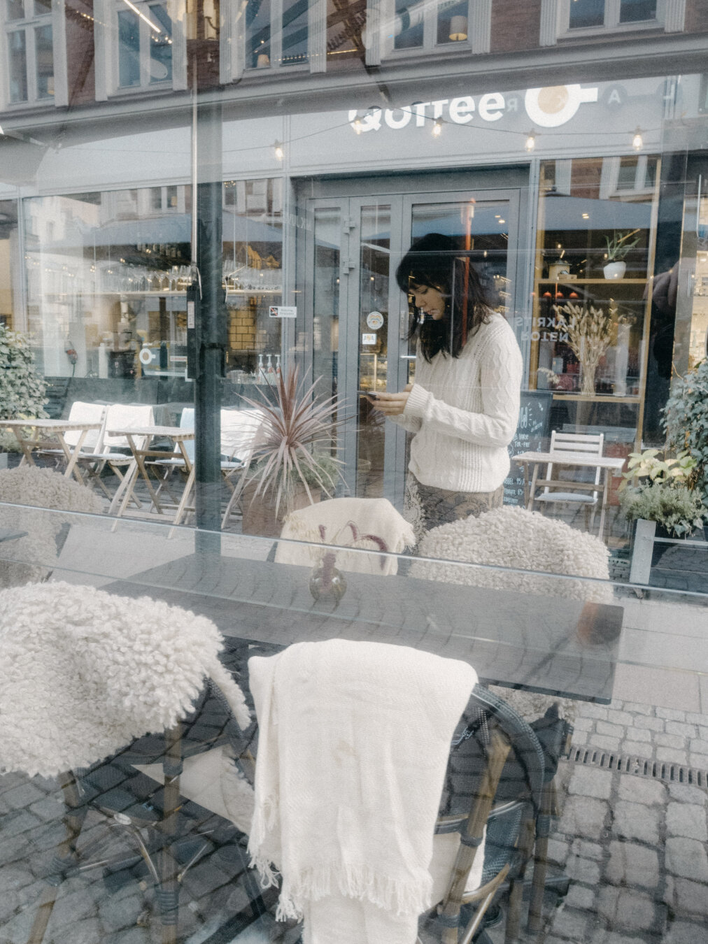 Street photograph taken in Malmö, Sweden during November. Warm café light creates high-contrast shadows against cool daylight, capturing a quiet coffee break scene. Rich color saturation and sharp street geometry shot on a compact digital camera.