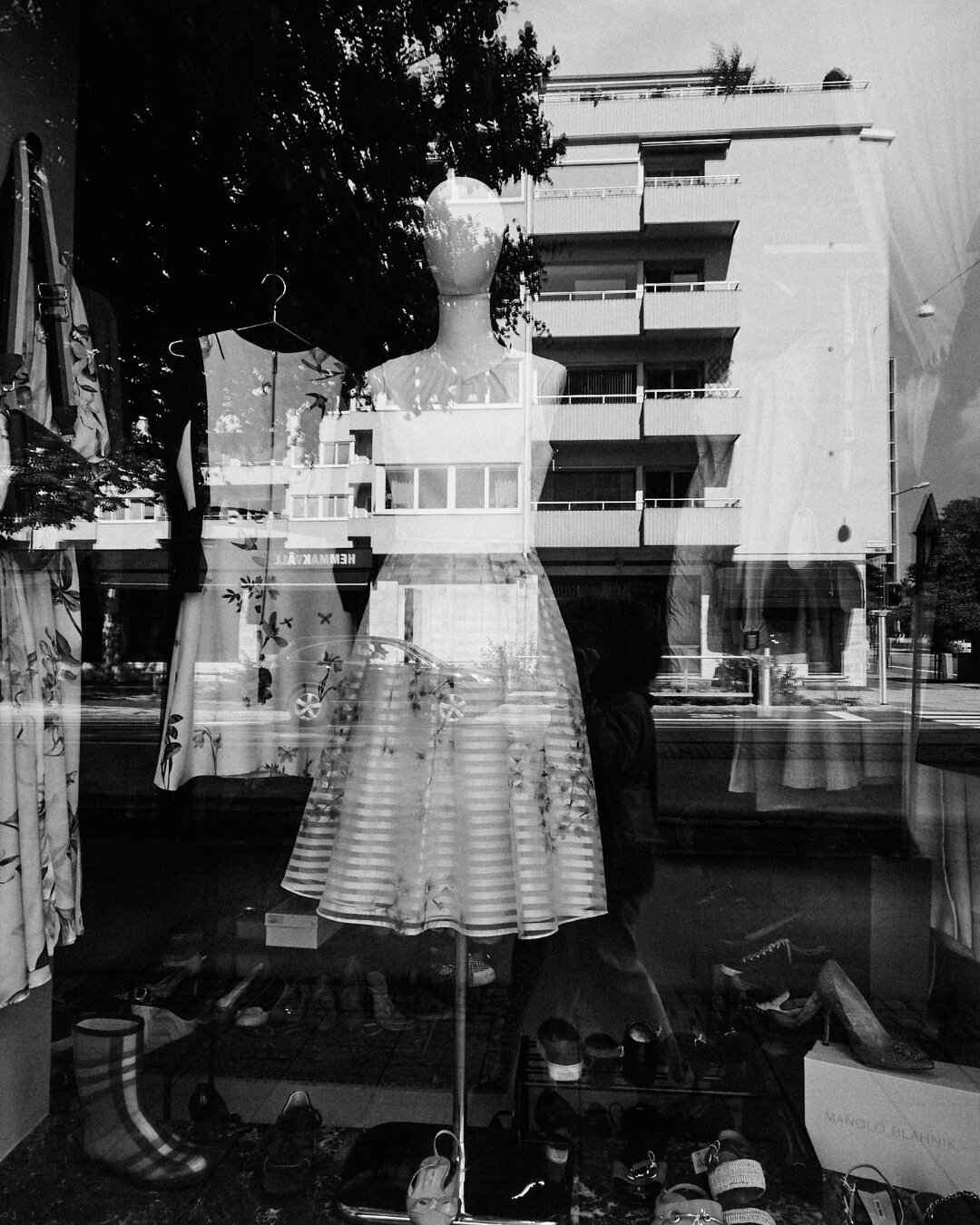 Storefront window reflection displaying a mannequin in a dress layered over an apartment building.