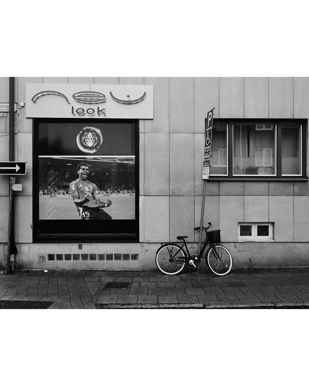 Flat view of a store window displaying a sports poster beside a bicycle parked against a tiled wall.