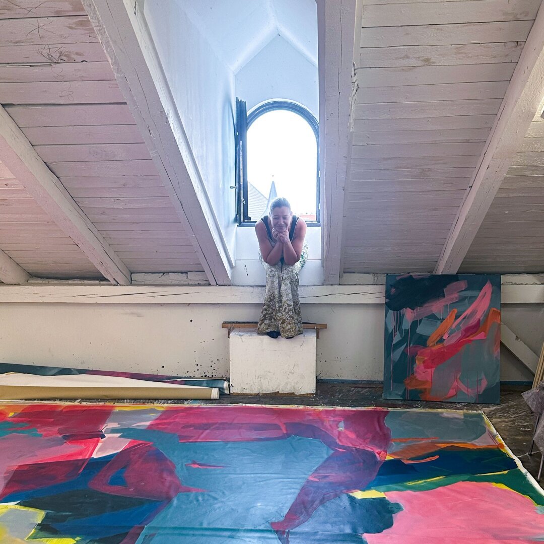 Artist sitting in small window watching her large painting on the floor