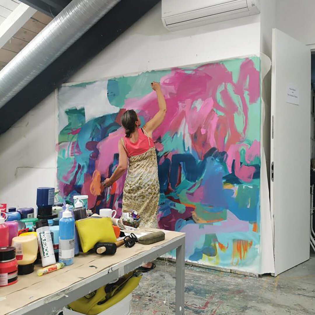 Artist painting a huge canvas on the wall, colors and art supplies in the front