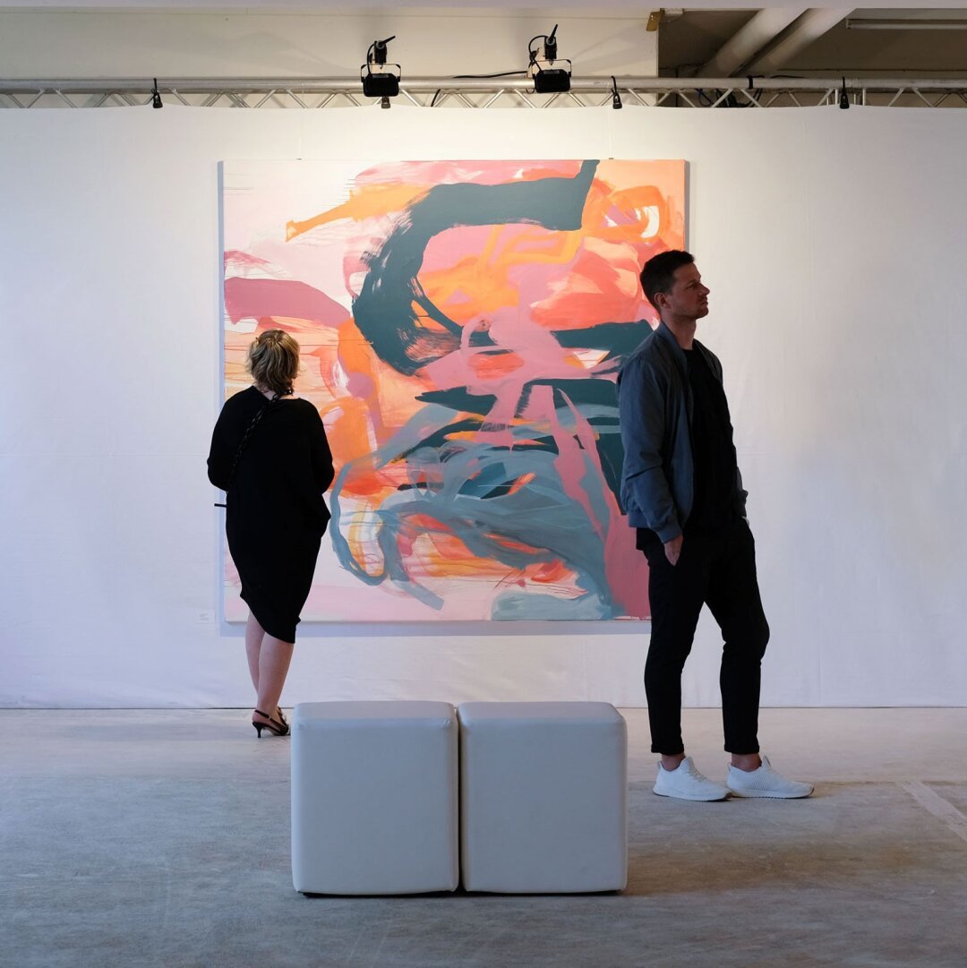 Two people, one in front of a large abstract painting watching it, the other person turned to the right, watching another painting