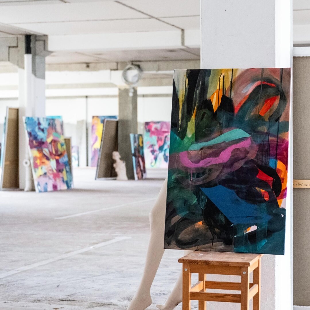 Abstract painting on chair in the front, many abstract paintings in the back in a big, empty loft